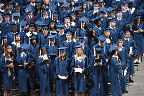graduates in wide angle  shot standing on arena floor in their cap and gowns